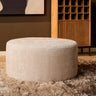 MySofa ronde poef 80 cm in beige chenille op een hoogpolig vloerkleed voor een houten wijnkast
